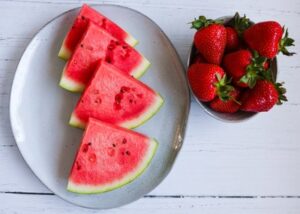 Slices of fresh watermelon on a plate with a bowl of strawberries