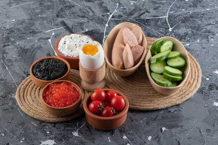 High-protein foods, including eggs, sausages, vegetables, and caviar, on a table.
