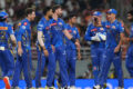 Cricket players in blue jerseys standing together on the field.