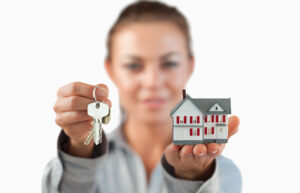 Person holding keys and a small house model.