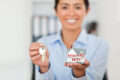 Woman holding house keys and miniature home model representing property purchase and home ownership concept