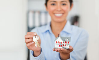 Woman holding house keys and miniature home model representing property purchase and home ownership concept