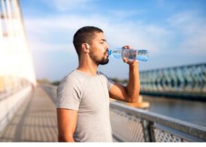 Man drinking water from a bottle after workout on a bridge, staying hydrated during exercise
