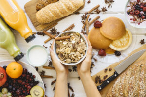 Top view of a person holding a bowl of raw millet grains, surrounded by gluten-free ingredients like fresh apples, eggs, and a 'Gluten-Free Diet' infographic.