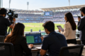 Sports professionals analysing match data and recording live coverage at a packed stadium, highlighting career opportunities in sports analytics and broadcasting.
